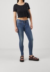 Czarny krótki t-shirt z detalami guzików, zestawiony z niebieskimi obcisłymi jeansami i brązowymi sandałami na paski z masywną podeszwą.