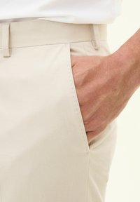 Pantaloni beige in un tessuto leggero, caratterizzati da una consistenza liscia, dettagli con tasche laterali e una vestibilità su misura con fronte piatto.