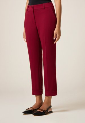 Woman wearing burgundy tailored cropped pants with cuffed hems and black pointed slingback flats with brown striped straps.