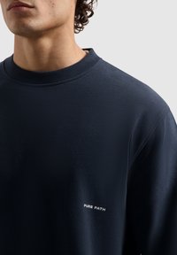 Marineblauwe sweatshirt van een gladde stof met een normale halslijn, met witte tekst "PURE PATH" op de linker onderzijde.