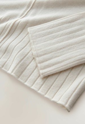 Raidallinen neulepaita vaaleanbeige. Siinä on pehmeä tekstuuri pystysuorilla viivoilla ja taitettu hihansuu. Materiaali näyttää mukavalta ja lämpimältä.