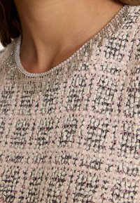 Roze en witte gebreide trui met een ronde halslijn en decoratieve zilveren kralen. De stof heeft een geweven patroon met verhoogde elementen.