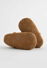 Chaussons en tissu marron avec un motif de visage d'ours, texture douce, forme arrondie et accents élastiques. Semelle imitation suède pour une bonne adhérence.