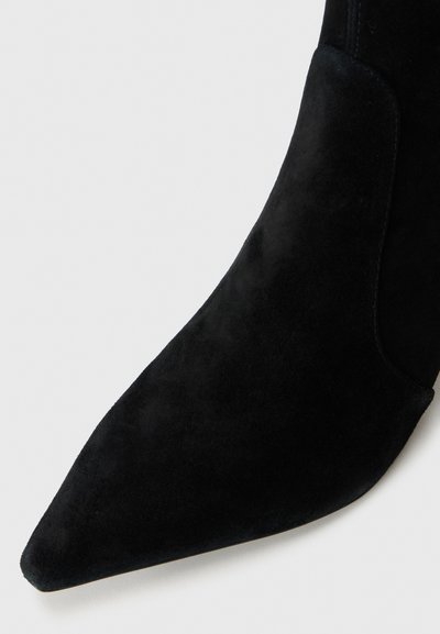 Svart mockaskor i ankellängd med spetsig tå och en slät yta. Designen har en elegant silhuett och inga synliga detaljer.