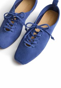 Blå mockaskor med snörning och utskuren detalj, mjukt material, rund tå och flexibel sula. Snörena är placerade i fram.