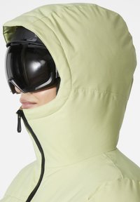 Hellgrüne isolierte Jacke mit Kapuze, mit einem Reißverschluss und schwarzen Skibrillen. Glatte Textur und minimalistische Design-Details.