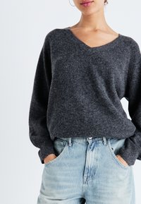 Maglione in maglia grigio carbone con scollatura a V e maniche a palloncino, abbinato a jeans alti di un blu chiaro. Tessuto morbido e vestibilità rilassata.