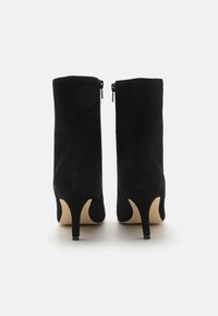 Bottes basses en daim noir au design élégant, avec un bout pointu et un talon aiguille de 7,5 cm. Fermetures éclair à l'arrière pour un enfilage facile.