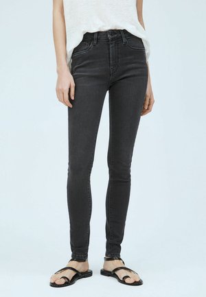 Jeans negros ajustados de denim con una cintura alta y un ligero desgaste. Combinados con sandalias negras minimalistas.