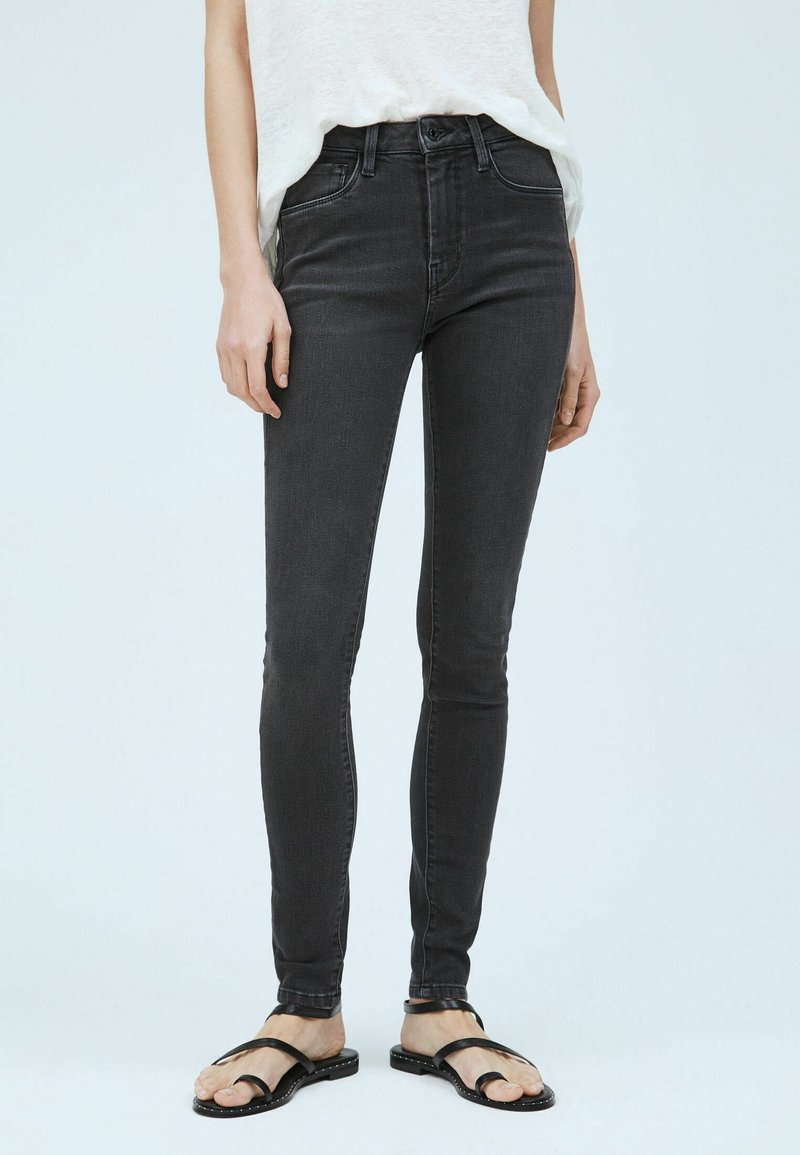 Jeans negros ajustados de denim con una cintura alta y un ligero desgaste. Combinados con sandalias negras minimalistas.