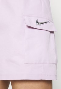 Světle fialové bavlněné šortky s boční kapsou a stříbrným logem Nike. Hladká textura a přizpůsobený design.