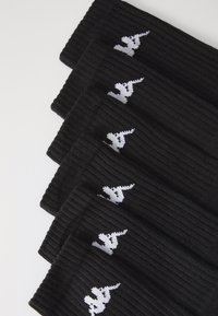 Calcetines negros con textura acanalada y un logo blanco. La tela parece suave y texturizada, con un patrón uniforme que se repite en múltiples pares.