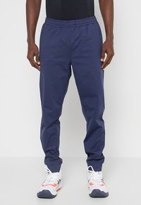 Granatowe dresy z elastyczną talią, zwężanymi nogawkami i teksturowanym wykończeniem materiału, połączone z białymi i pomarańczowymi butami sportowymi.