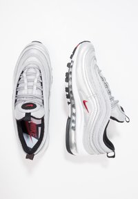 Tenisky Nike Air Max 97 ve stříbrné barvě. Mají síťovinu a syntetické materiály, výrazný vlnitý vzor, červený akcent s logem, průhledné vzduchové tlumení a černou podrážku.