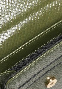 Olive green textured faux leather wallet with a shiny finish, featuring a gold-tone snap closure and a black patterned interior lining.