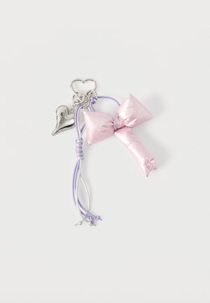 Porte-clés avec un nœud rose brillant, relié par des cordons lavande et argent, orné d'un charm en forme de cœur brillant, le tout sur un fond blanc.