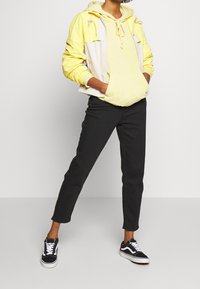 Gul och ljusgrå zip-jacka över en gul hoodie, kombinerad med svarta byxor och svarta sneakers med vita detaljer. Avslappnad outfit.