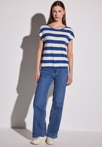 Camiseta de rayas en azul y blanco, de manga corta, con un ajuste relajado. Combinada con jeans de pierna ancha en azul claro y zapatillas blancas. Textura de tela suave.