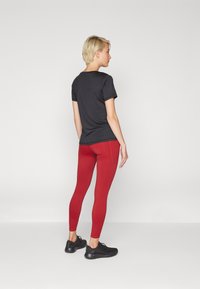 T-shirt noir à manches courtes, leggings rouges ajustés et chaussures de sport noires. Tissu lisse, coupe slim, couleurs contrastées et détails de couture minimaux.