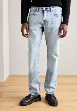 Light blue denim jeans with a straight cut, slight fade, and five-pocket design. Paired with black loafers and a black sweater.