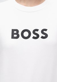 Λευκό πουκάμισο με τη λέξη BOSS τυπωμένη με μεγάλα μαύρα κεφαλαία γράμματα στο στήθος.