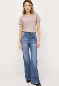 T-shirt rosa chiaro a maniche corte abbinata a jeans blu a vita alta e svasati. L'outfit presenta tasche in denim e una texture di tessuto liscia.