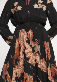 Robe noire à manches longues et taille froncée, avec des motifs mythiques de lions et de fleurs rouges et beiges.