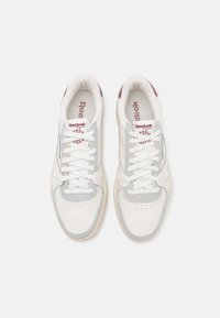 Vita och grå sportskor med övre i mocka och mesh, vita snören och en vinröd logga på tungan. Gummisula med perforeringar.