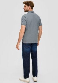 Polo gris à manches courtes, porté avec un jean bleu foncé et des baskets blanches. Le dos présente un design uni, sans logos visibles.