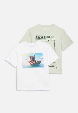 Deux t-shirts à manches courtes, l'un blanc avec un tigre surfant et le texte "SURFER DUDE", l'autre vert clair avec "FOOTBALL GOAAAAAL !" et un graphique de but.