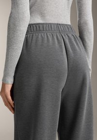 Szürke melegítőnadrág elasztikus derékpánttal, hátulról bemutatva. Az anyag puha, sima tapintású és enyhén fényes.