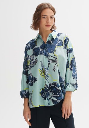 Camicia a stampa floreale in azzurro chiaro, con accenti in blu scuro e giallo neon. Maniche lunghe con polsini e chiusura con bottoni.