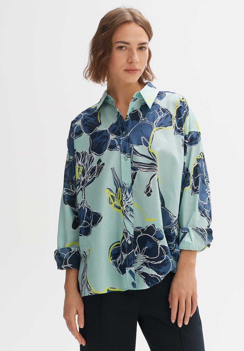 Camicia a stampa floreale in azzurro chiaro, con accenti in blu scuro e giallo neon. Maniche lunghe con polsini e chiusura con bottoni.