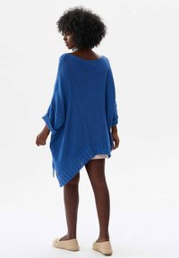 Blauwe oversized gebreide trui met een brede halslijn en losse mouwen, met een diagonale zoom en geribbelde accenten.