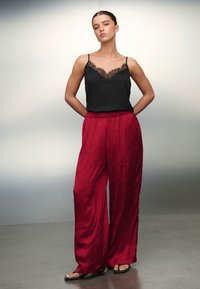 Haut noir sans manches avec bordure en dentelle et pantalon rouge à jambes larges au tissu froissé, assorti de sandales noires. Design simple et élégant.