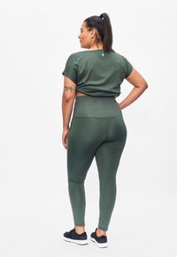 Groene sportoutfit bestaande uit een korte mouwen crop top en hoge taille leggings. Gladde textuur met een aansluitend ontwerp, gecombineerd met zwarte sneakers.