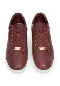 Sneakers in pelle borgogna con texture liscia, punta rotonda, suola in gomma bianca e occhielli in tono oro con dettagli coordinati nei lacci.