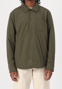 Olivengrøn skjorte med knapper, spidst krave, enkelt brystlomme og trykknapper. Fremstillet af letvægtstof med en glat tekstur.