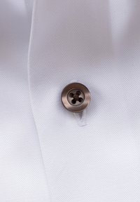 Tumepruun neljaauggeline nupp, mis on õmmeldud valgele tekstuursele kangale, kus on nähtavad nööpaugutikkimised lähedal.