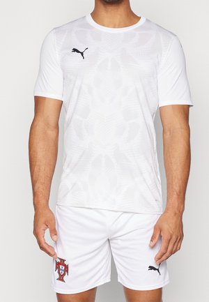 Mand iført hvid Puma sportstrøje og shorts med det portugisiske fodboldholds emblem på shortsene.