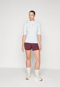 Lys blå kortermet rash guard sammen med burgunder treningsshorts. Antrekket har en tettsittende design og glatt, elastisk stoff.