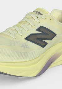 Αθλητικό παπούτσι New Balance ανοιχτού κίτρινου χρώματος με υφασμάτινο επάνω μέρος, γκρι λογότυπο στο πλάι, παχιά επενδυμένη σόλα και λευκά κορδόνια.