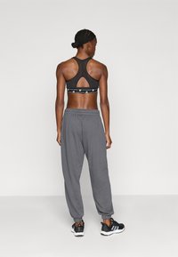 Črni športni modrček z izrezom na hrbtu, sive trenirke z elastičnimi manšetami in črni športni copati z belimi črtami.