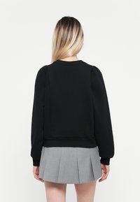 Sweatshirt noir avec des épaules bouffantes et un ourlet côtelé, associé à une jupe plissée grise. Tissu lisse avec un design simple.