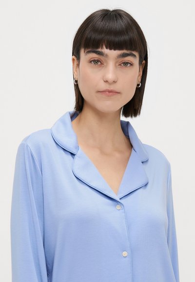 Camisa de pijama azul-claro com gola, fecho de botão e textura suave. Apresenta mangas longas e um design de corte amplo.