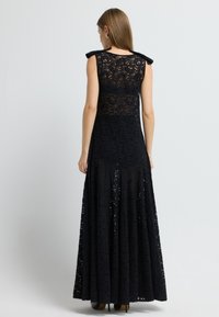 Sorte blond maxi-kjole med tætsiddende liv, udvidet nederdel og skulderdetaljer. Har detaljerede blomster mønstre og en semi-gennemsigtig ryg.