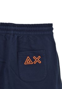 Pantaloni da tuta blu navy con vita elastica e un triangolo arancione ricamato con una "X" sulla tasca posteriore. Tessuto morbido.