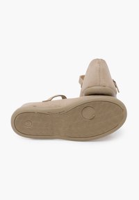 Zapato de ante beige con punta redondeada y un tacón pequeño. Cuenta con una suela de goma texturizada con un agarre con patrón y una correa ajustable.