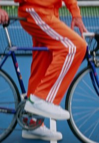 Białe trampki z zielonymi akcentami, pomarańczowy dres z białymi paskami oraz niebieski rower, z naciskiem na obuwie i odzież.