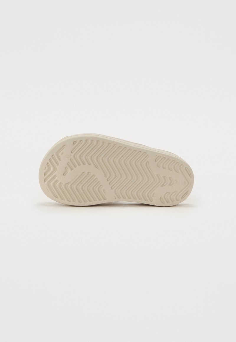 Beige Sneaker-Sohle mit einem Zickzack-Muster, die einen leicht erhöhten Rand und eine glatte, matte Textur aufweist. Gummi-Material, das für Traktion sorgt.
